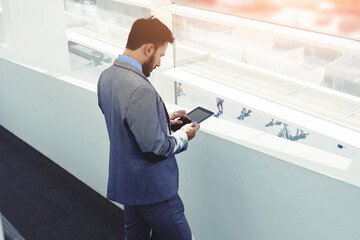 Half length portrait of rich businessman holding portable digital tablet during work break in hallway