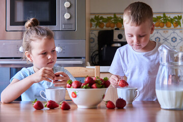 Two beautiful children in the kitchen eating strawberries and drinking milk.Children have fun. 