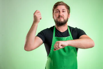 Supermarket employee with green apron and black t-shirt showing time is money gesture