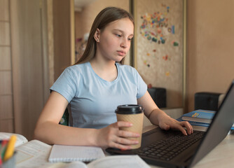 Teen girl, home lessons at a laptop, a cup of coffee tea, watching videos, learning lessons, home education, preparing for an exam at the institute and school. Qualification courses, video conference