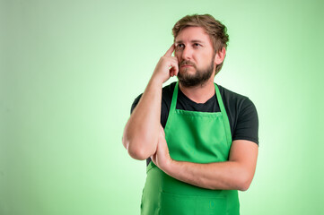 Supermarket employee with green apron and black t-shirt wondering