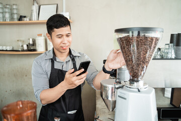 male barista using smartphone to check new orders of coffee