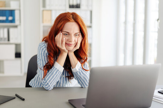 Red-haired woman in office looking at laptop