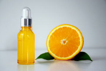 Cosmetic bottle with Vitamin C serum and half of orange on white background. Citrus essential oil, cosmetics aromatherapy. Face care, treatment, anti-aging, cosmetic industry concept.