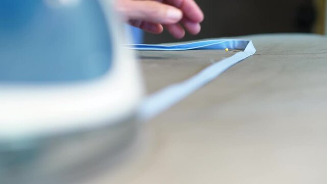 Elderly woman ironing a cotton face mask strap with a yellow pin laying on an ironing board.