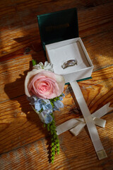 two wedding rings in a box on a wooden background and a rose lies nearby