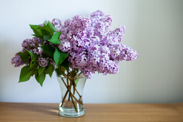 Bouquet of lilac lilacs in a glass transparent vase stands on a wooden tabletop