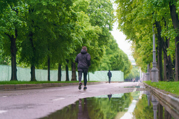 Gorky Park (Neskuchny Garden) - popular place for walking of citizens. Rainy summer day. Coronavirus pandemic. Sports allowed by the authorities. Young man in black clothes jogging