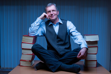 Cheerful businessman sitting on a desk between stacks of books