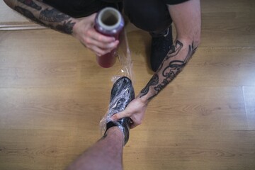 High angle shot of a tattoo artist wrapping the client's foot in plastic wrap