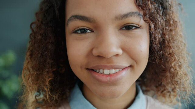 Slow motion headshot portrait of attractive Afro-American girl teenager smiling at home looking at camera. Positivity, emotions and people concept.