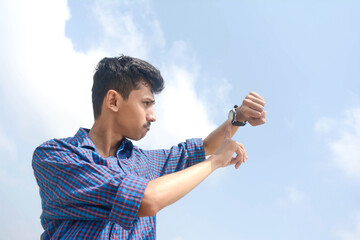 Portrait of young man looking at his watch. isolated on sky background.