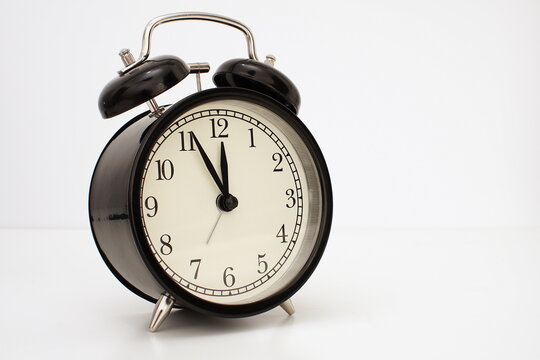 Black vintage alarm clock on table. White background. Wake up concept. An image of a retro clock showing 11:55 pm/am.  
