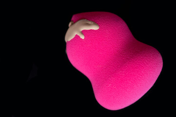 Pink make up sponge with foundation on black background. Copy space
