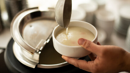 a mans hand holds a ladle and puts on the  soup ,A man pouring  soup into white dish from  tureen