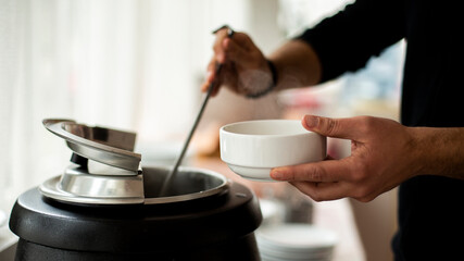 Fototapeta na wymiar a mans hand holds a ladle and puts on the soup ,A man pouring soup into white dish from tureen