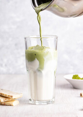 Pouring matcha latte into a glass with coconut milk. White chocolate on wooden and marble background