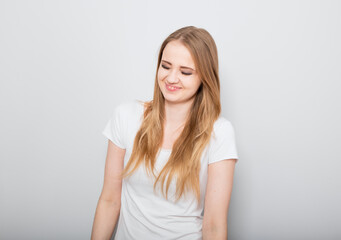 Pretty smiling joyful young woman with fair blond long hair in casual dress looking with happy. Studio shot of good looking beautiful woman isolated against grey studio wall