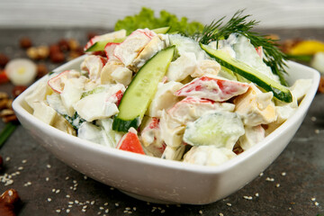 Fresh vegetable salad with mayonnaise in a square white plate. On a gray concrete textured background