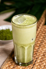 Glasses of matcha latte with coconut milk and white chocolate on marble background. Tropical monstera leaf