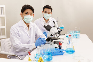 Fototapeta premium Two Male Scientists wear Face Mask working in Lab while Looking at Camera and Ready to Work and Presentation. Blue Tone. SARS-CoV-2 , Covid-19 THEME.
