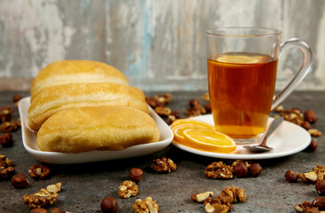 Fresh aromatic pastries for breakfast or snack on a square white plate, 
a cup of tea with lemon