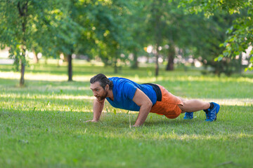 Fototapeta na wymiar Middle aged man doing push-ups on the grass in park.