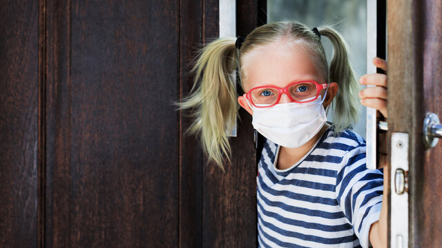 Little child looking out opened door after staying at home due banned street activity. Kid wearing medical face masks go out for outside walk. Ending coronavirus Covid-19 disease quarantine.