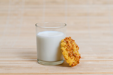 A round shortbread cookie with peanuts stands next to a full glass of milk.