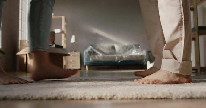 Close-up low angle shot of legs of a cute couple walking barefoot on floor of their new home. Girl standing on tip-toes to kiss her boyfriend - love, new life concept 4k footage
