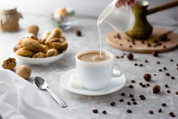 a woman's hand takes a milk jug and pours milk into the coffee from above
