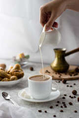 a woman's hand takes a milk jug and pours milk into the coffee from above