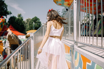 Beautiful brunette girl in an amusement park in pin-up style on the background of carousels with...