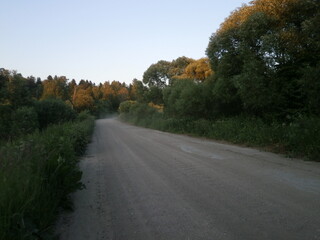 
A traditional Russian landscape with a rolled primed road going into perspective, evening time of the day, sunset, ideas for creating websites, presentations, printing on postcards, magnets. 