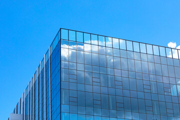 Fototapeta na wymiar Part of a glass mirrored office building reflecting the blue sky. Exterior decoration of a hotel or shopping center with modern materials.