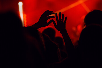 Silhouette of raised hands at a music concert. Red tinted