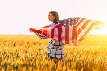 Attractive young happy woman, in a wheat field with an American flag on the background of the sunset