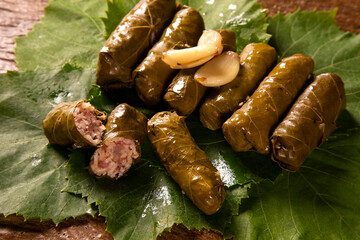 Sarma - Rice and mint wrapped in grape vine leaves on wood background.