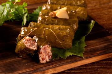 Sarma - Rice and mint wrapped in grape vine leaves on wood background.