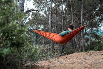 Man stretched out in a hammock while using his mobile