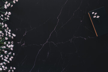 Flat lay of a floral arrangement and a wood piece and a book against black marble