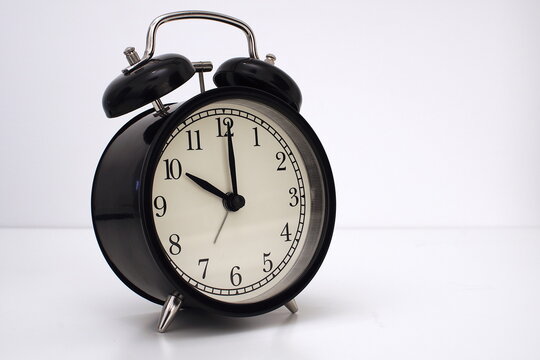 Black vintage alarm clock on table. White background. Wake up concept. An image of a retro clock showing 10:00 pm/am.  