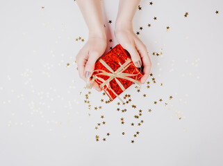 Female's hands with gift box on white background with golden confetti stars New Year concept 2021