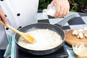 Chef pouring fresh milk the pan for cooking mushroom cream soup