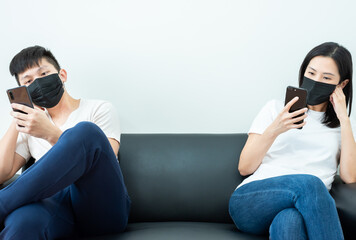 Fototapeta premium An Asian couple stays together and playing the phone with black mask and social distancing.