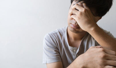 closeup man sitting alone felling sad worry regret or fear and hand off his face in the room. soft-focus and over light in the background