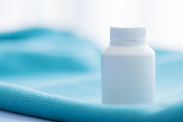 A white medicine bottle on the green bed sheet.