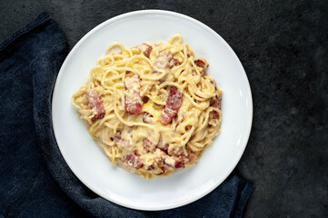 Homemade carbonara pasta in a white plate on a stone background