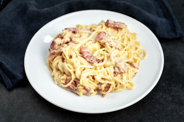 Homemade carbonara pasta in a white plate on a stone background
