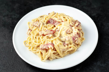 Homemade carbonara pasta in a white plate on a stone background